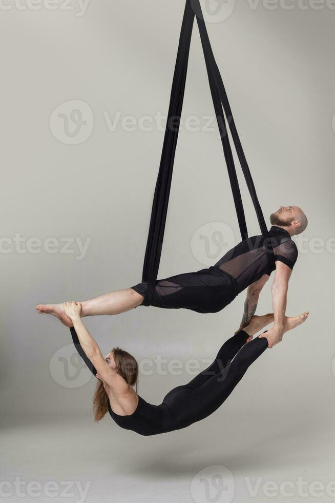 Beautiful girl and an athletic man in a black sport suits are performing an acrobatic elements in a studio. photo