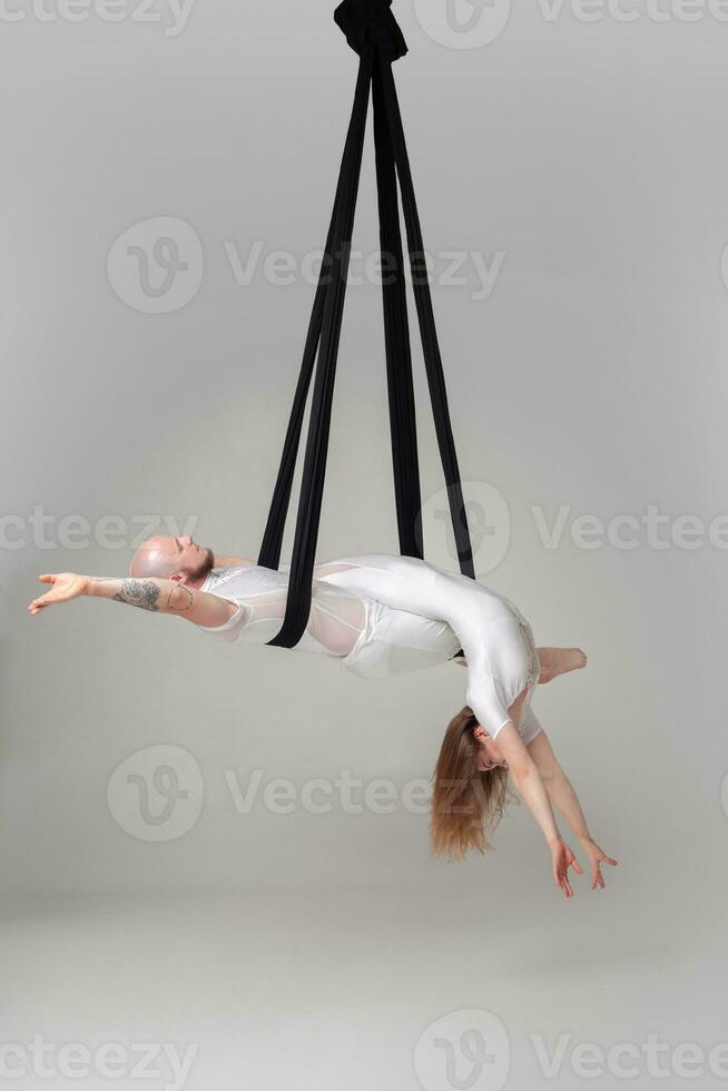 Beautiful girl and an athletic man in a white sport suits are performing an acrobatic elements in a studio. photo