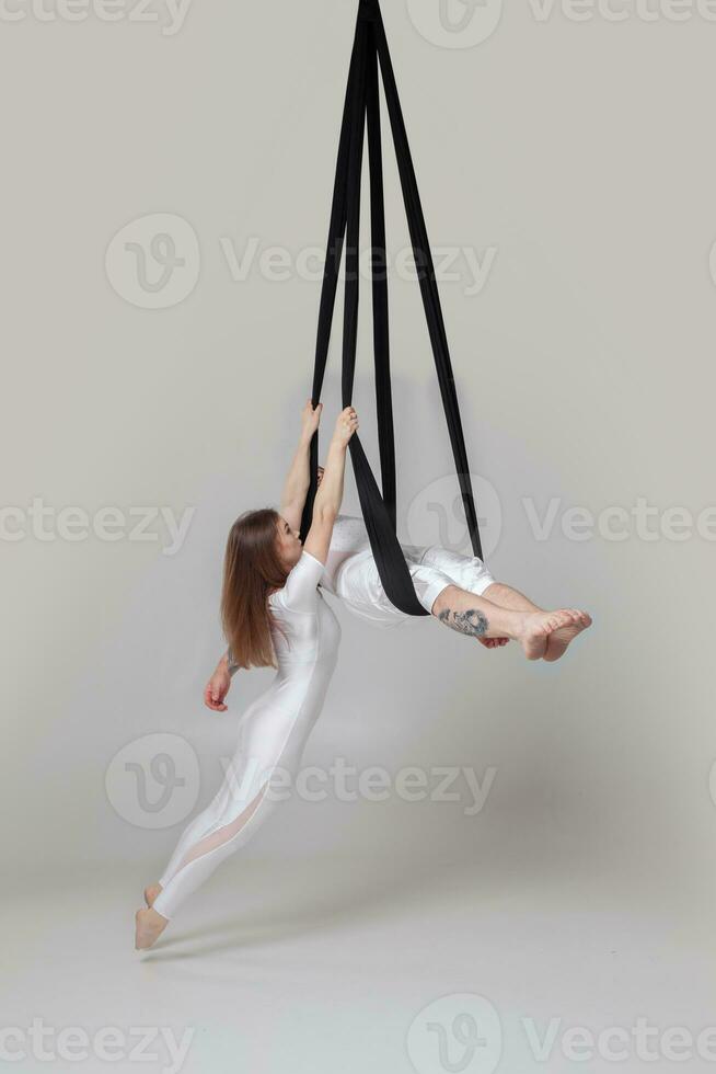 Beautiful girl and an athletic man in a white sport suits are performing an acrobatic elements in a studio. photo
