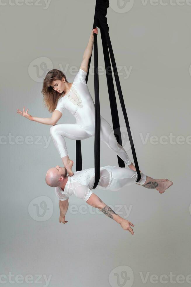 Beautiful girl and an athletic man in a white sport suits are performing an acrobatic elements in a studio. photo