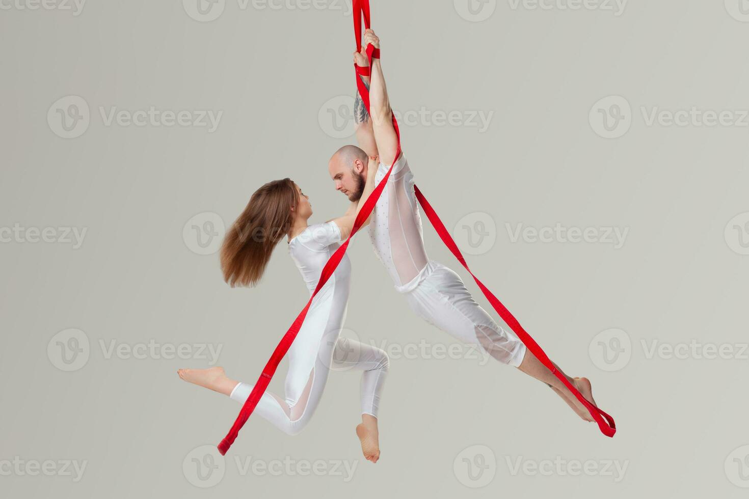 Beautiful girl and an athletic man in a white sport suits are performing an acrobatic elements in a studio. photo