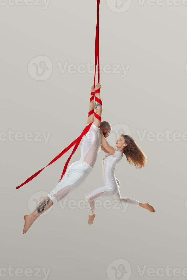 Beautiful girl and an athletic man in a white sport suits are performing an acrobatic elements in a studio. photo