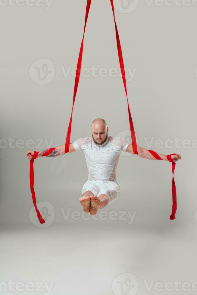 Athletic man in a white sport suit is performing an acrobatic elements in a studio. photo