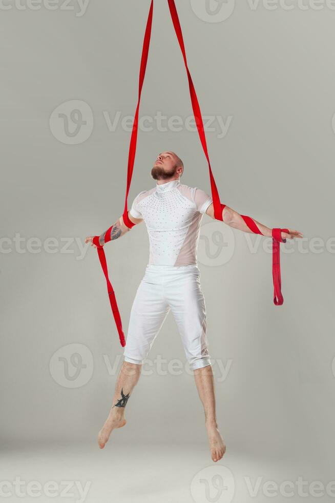 Athletic man in a white sport suit is performing an acrobatic elements in a studio. photo