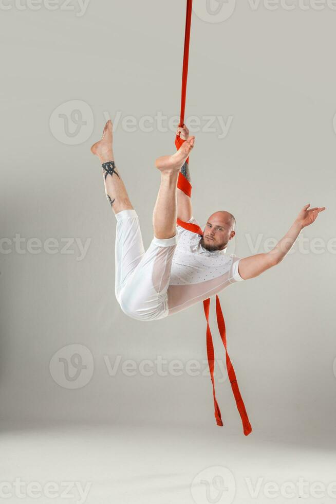 Athletic man in a white sport suit is performing an acrobatic elements in a studio. photo