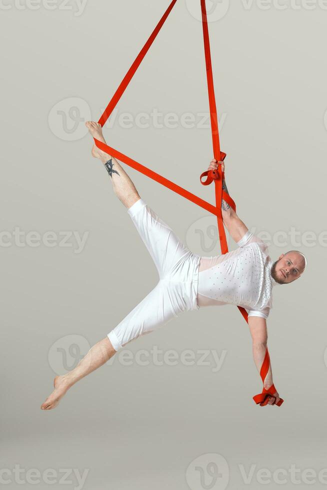 Athletic man in a white sport suit is performing an acrobatic elements in a studio. photo