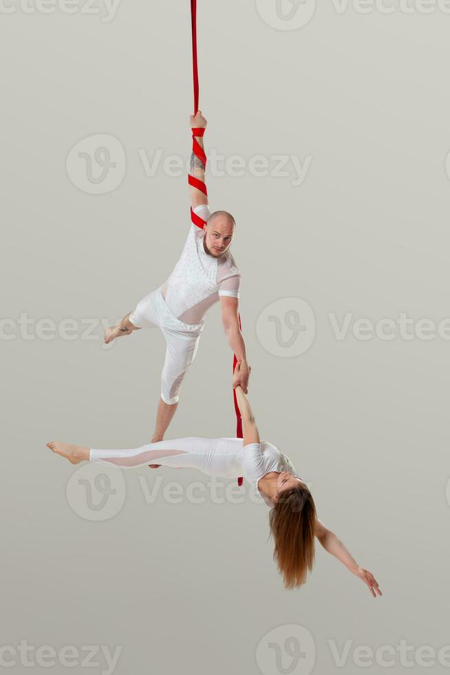 Beautiful girl and an athletic man in a white sport suits are performing an acrobatic elements in a studio. photo