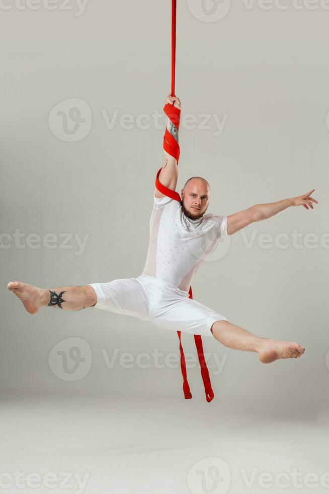 Athletic man in a white sport suit is performing an acrobatic elements in a studio. photo