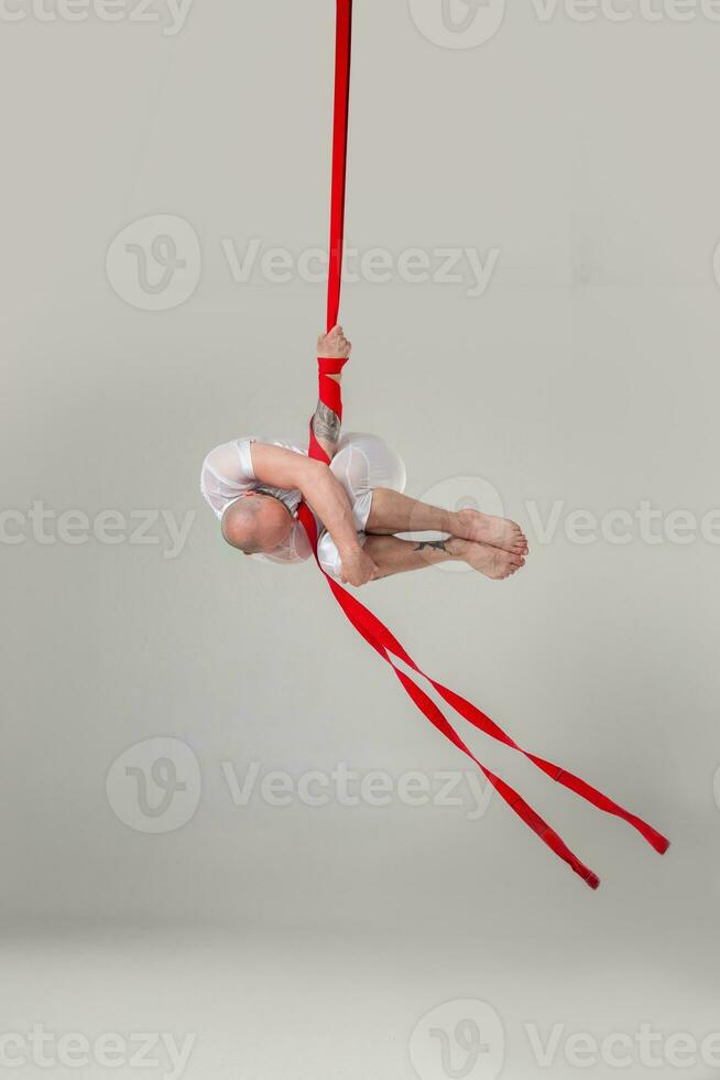 Athletic man in a white sport suit is performing an acrobatic elements in a studio. photo