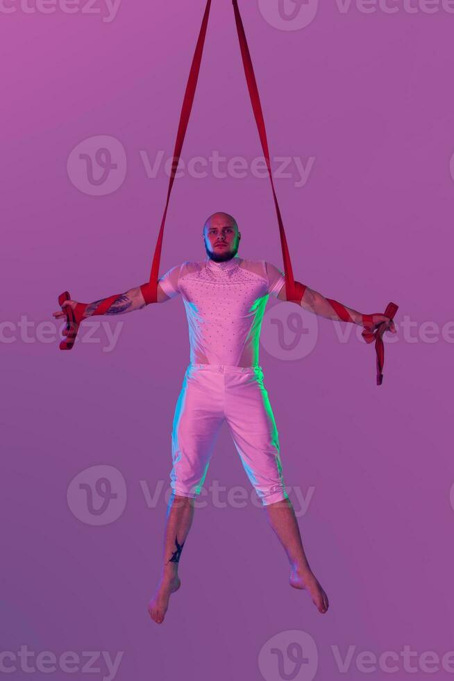 Athletic man in a white sport suit is performing an acrobatic elements in a studio. photo