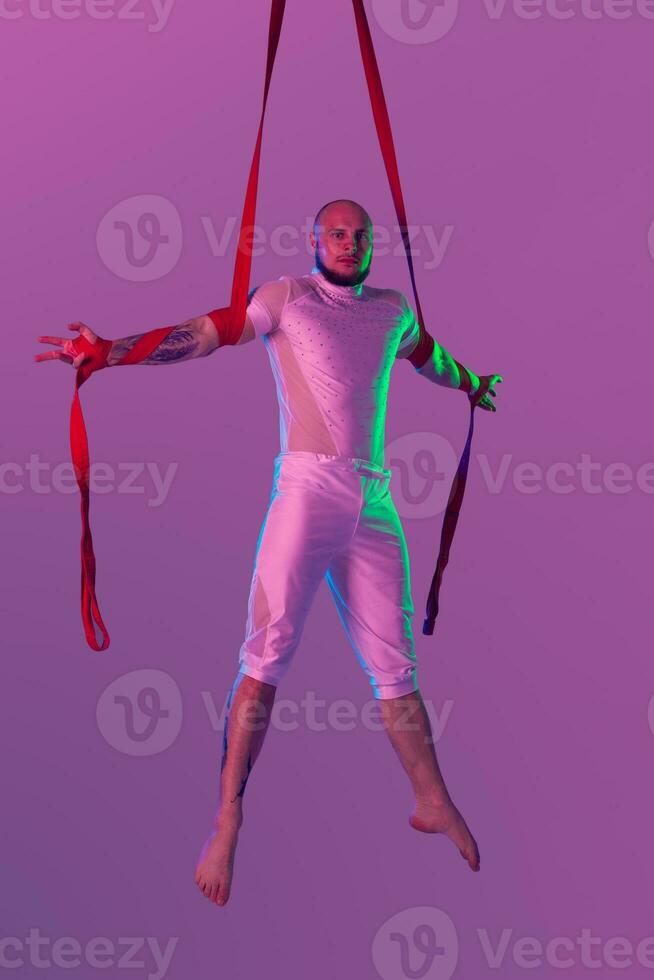 Athletic man in a white sport suit is performing an acrobatic elements in a studio. photo