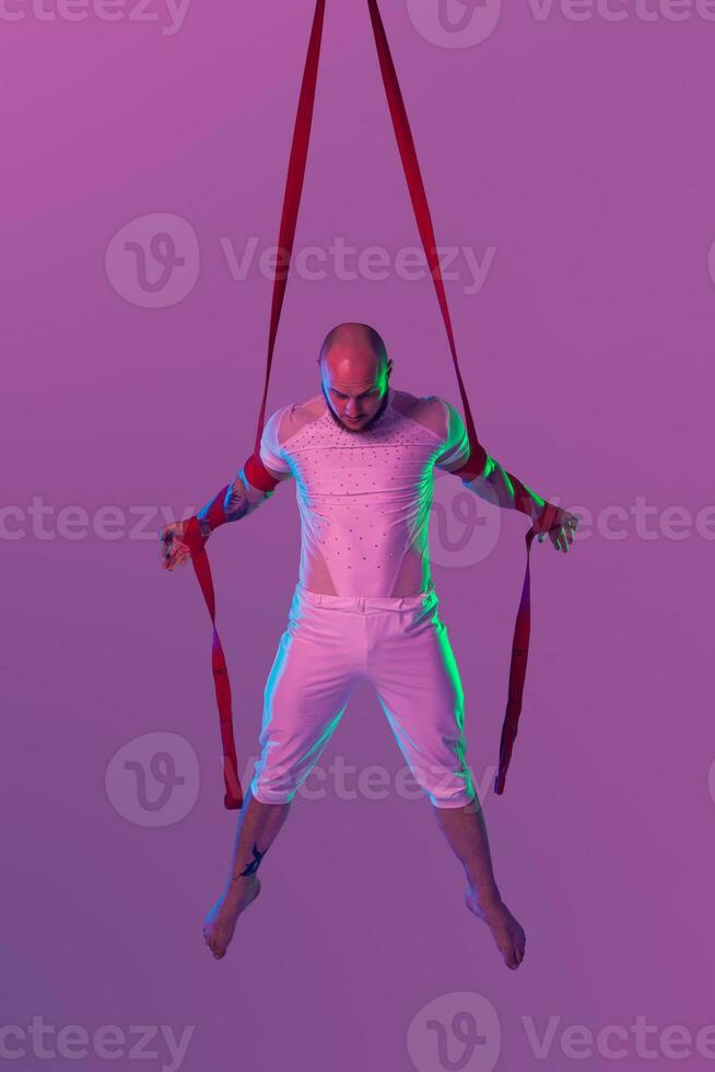 Athletic man in a white sport suit is performing an acrobatic elements in a studio. photo