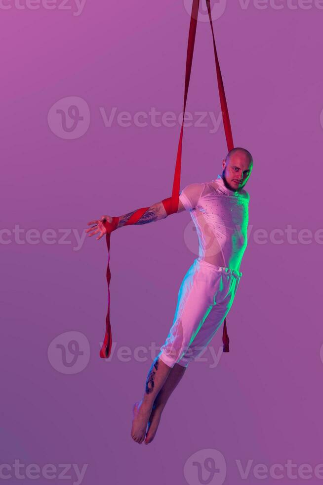 Athletic man in a white sport suit is performing an acrobatic elements in a studio. photo