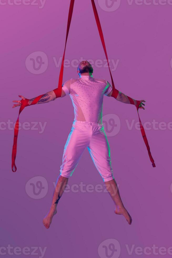 Athletic man in a white sport suit is performing an acrobatic elements in a studio. photo
