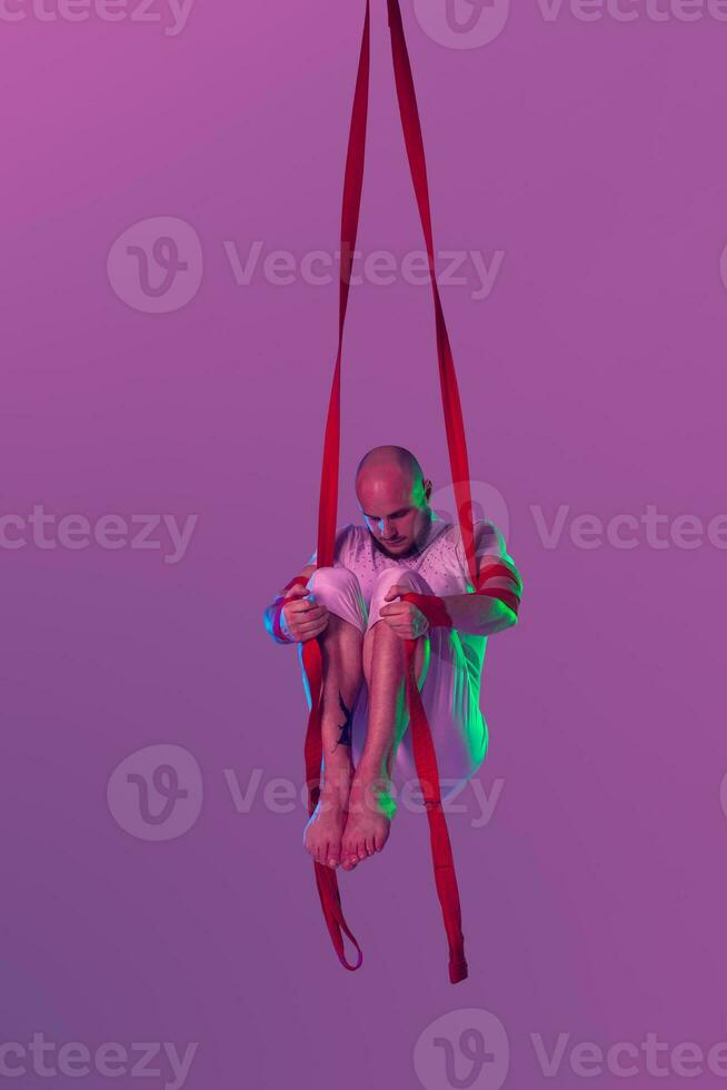 Athletic man in a white sport suit is performing an acrobatic elements in a studio. photo