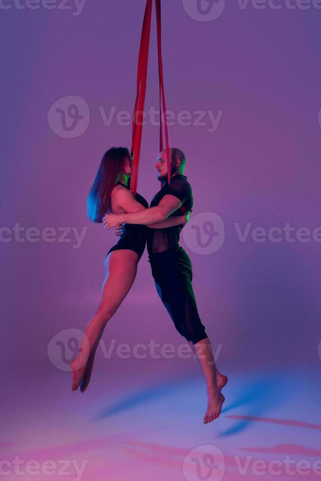 Beautiful girl and an athletic man in a black sport suits are performing an acrobatic elements in a studio. photo