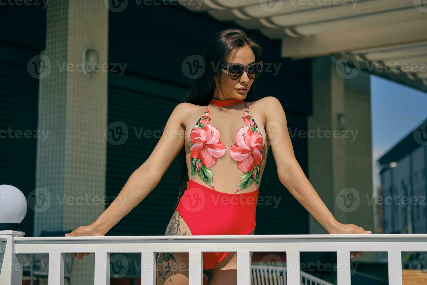 Portrait of a woman having rest in a recreation center or hotel with a swimming pool. Dressed in a colorful swimsuit and sunglasses. photo
