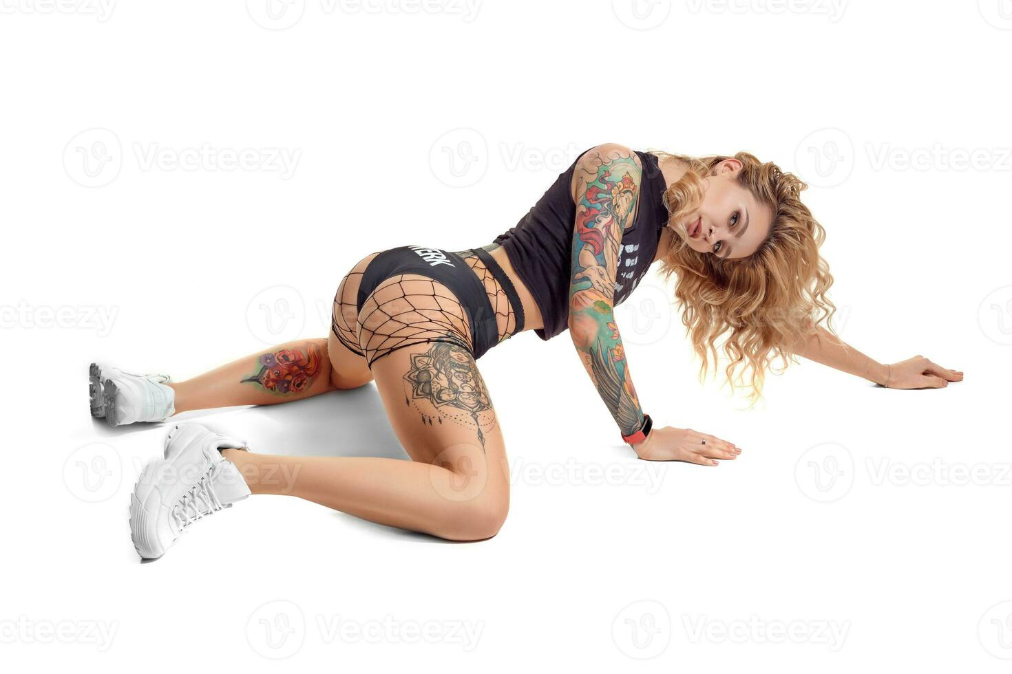 Sexy blond twerk woman with tattoed body and long curly hair is posing in studio. photo