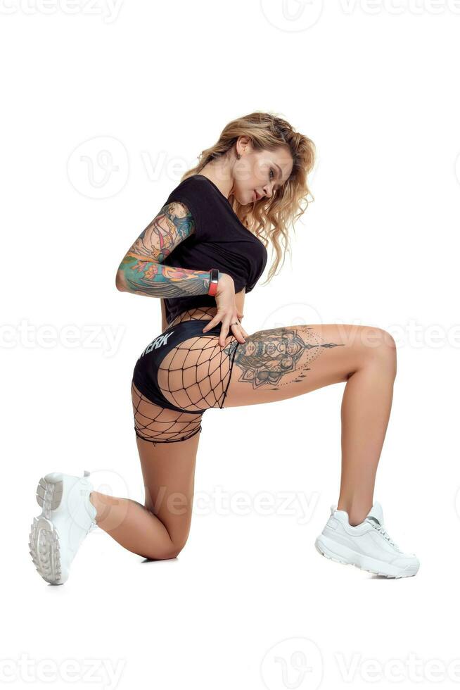 Sexy blond twerk woman with tattoed body and long curly hair is posing in studio. photo