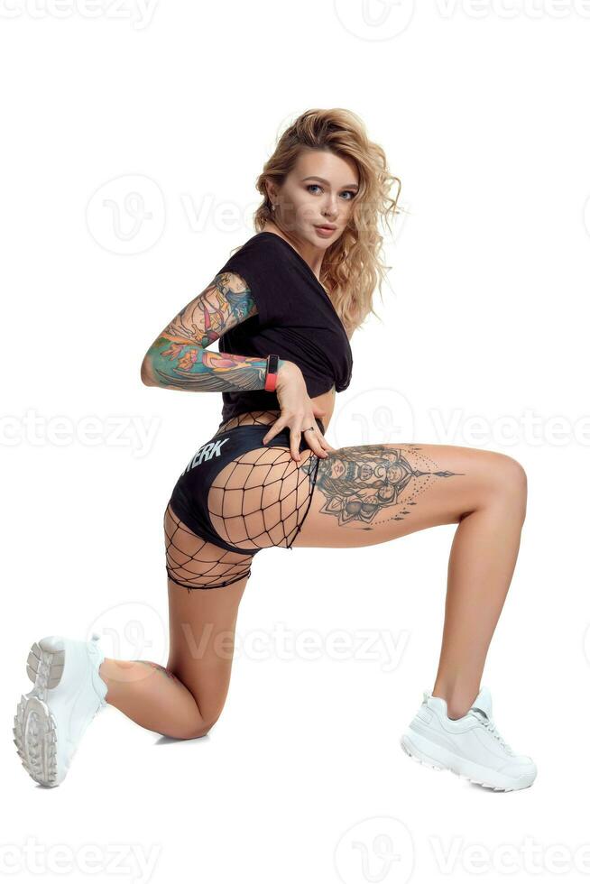 Sexy blond twerk woman with tattoed body and long curly hair is posing in studio. photo