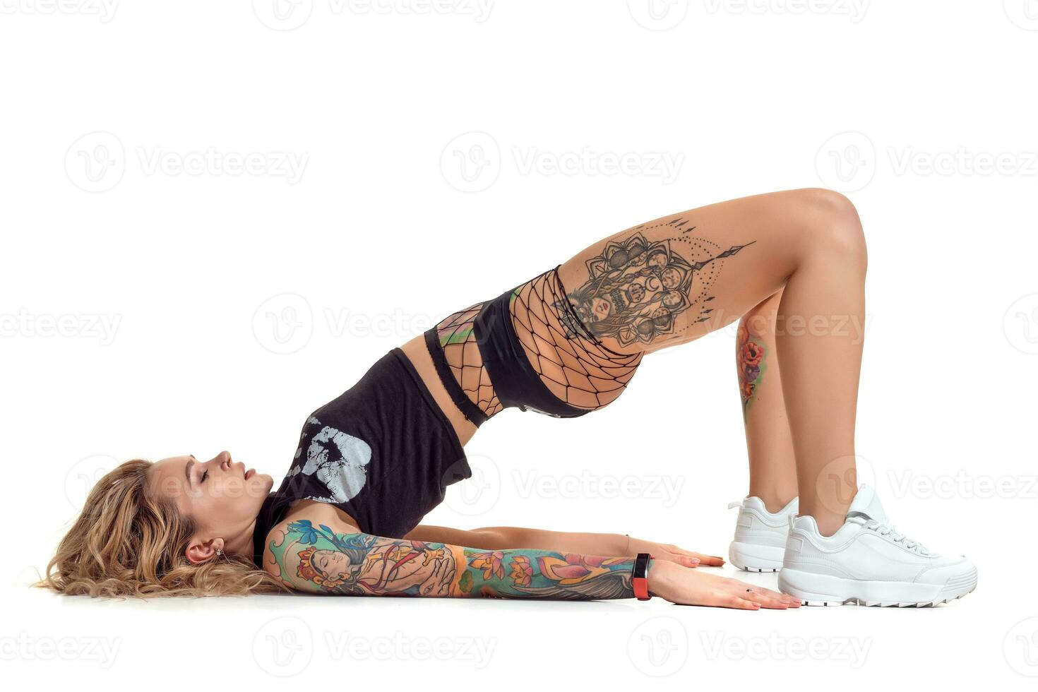 Sexy blond twerk woman with tattoed body and long curly hair is posing in studio. photo