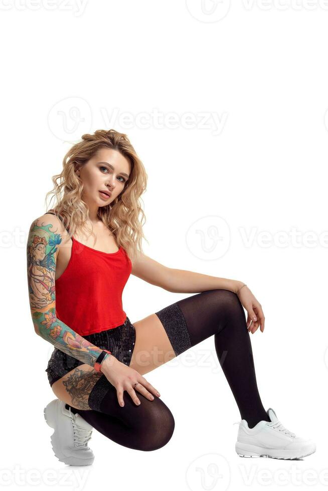 Sexy blond twerk woman with tattoed body and long curly hair is posing in studio. photo