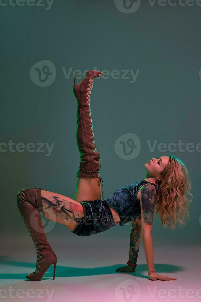 Sexy blond woman with tattoed body and long curly hair is dancing twerk in studio. photo