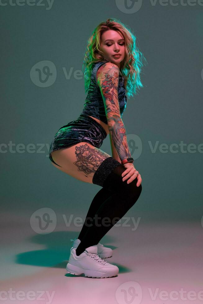 Sexy blond woman with tattoed body and long curly hair is dancing twerk in studio. photo