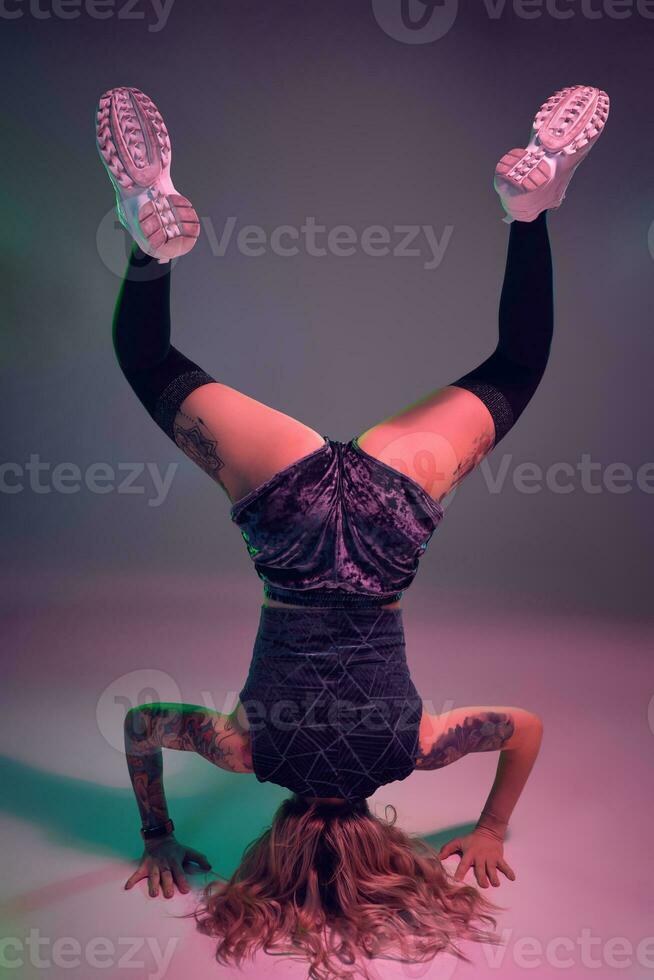 young beautiful blonde gymnast girl in velour blue booty shorts and black stockings standing upside down on pink background photo