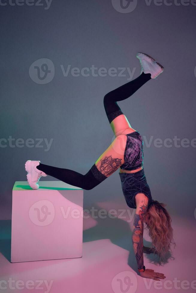 young beautiful blonde gymnast girl in velour blue booty shorts and black stockings standing upside down on pink background photo