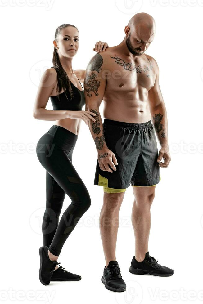 Athletic man in black shorts and sneakers with brunette woman in leggings and top posing isolated on white background. Fitness couple, gym concept. photo