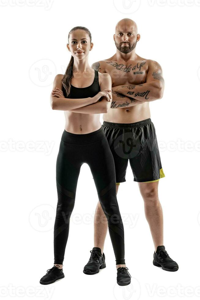 Athletic man in black shorts and sneakers with brunette woman in leggings and top posing isolated on white background. Fitness couple, gym concept. photo