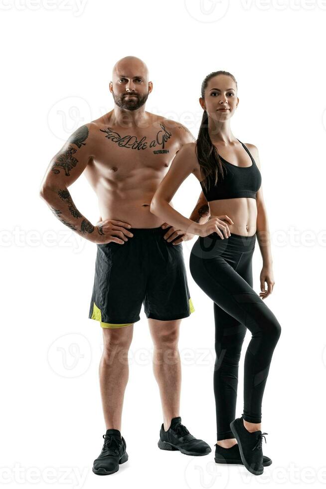 Athletic man in black shorts and sneakers with brunette woman in leggings and top posing isolated on white background. Fitness couple, gym concept. photo