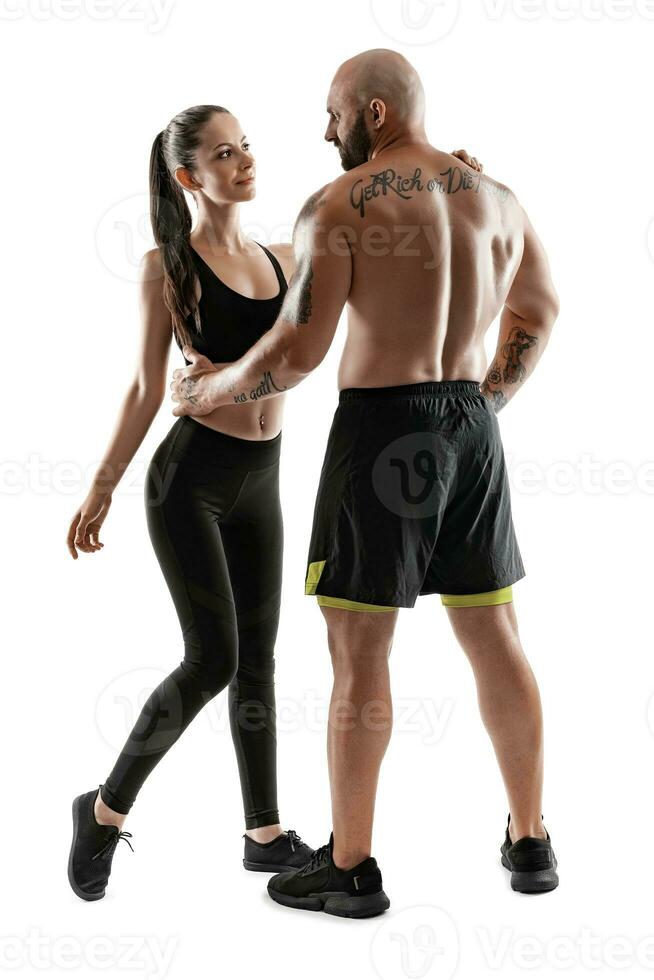 Athletic man in black shorts and sneakers with brunette woman in leggings and top posing isolated on white background. Fitness couple, gym concept. photo