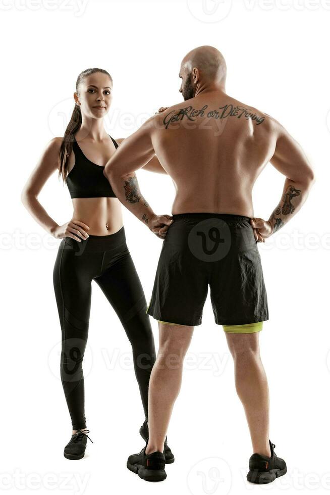 Athletic man in black shorts and sneakers with brunette woman in leggings and top posing isolated on white background. Fitness couple, gym concept. photo