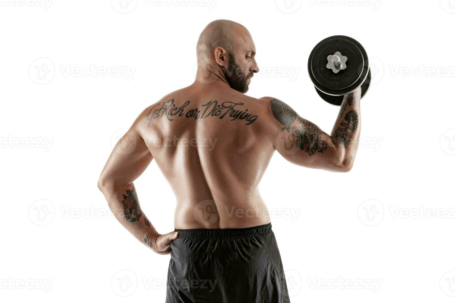 Athletic bald, tattooed man in black shorts is posing with a dumbbell isolated on white background. Close-up portrait. photo