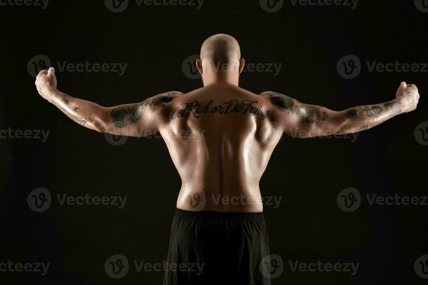 Athletic bald, bearded, tattooed man in black shorts is posing against a black background. Close-up portrait. photo