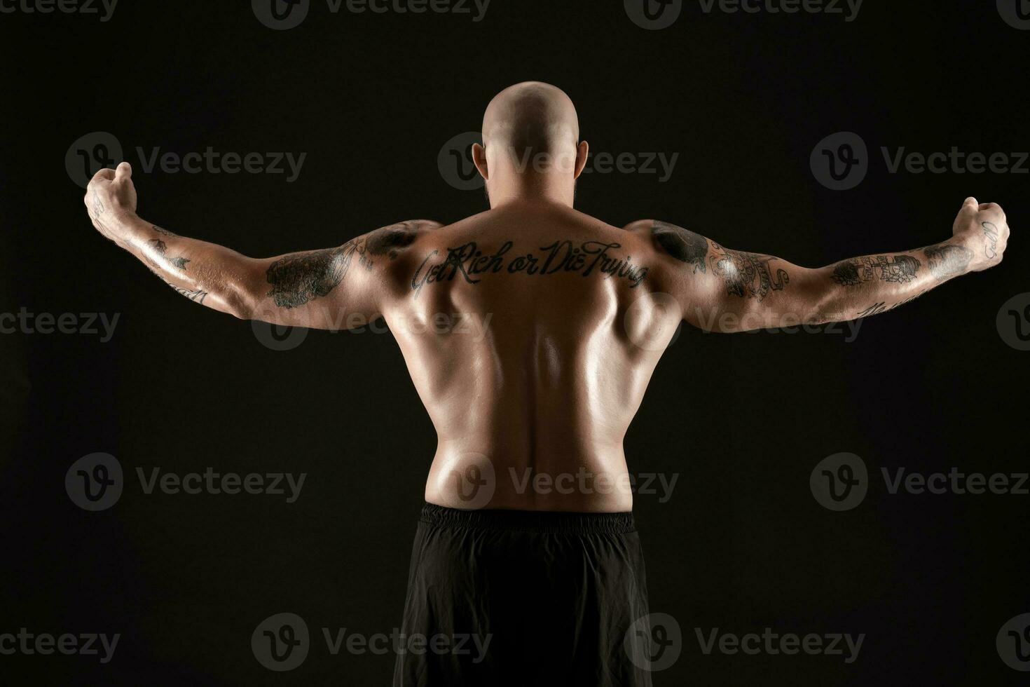 atlético calvo, barbado, tatuado hombre en negro pantalones cortos es posando en contra un negro antecedentes. de cerca retrato. foto