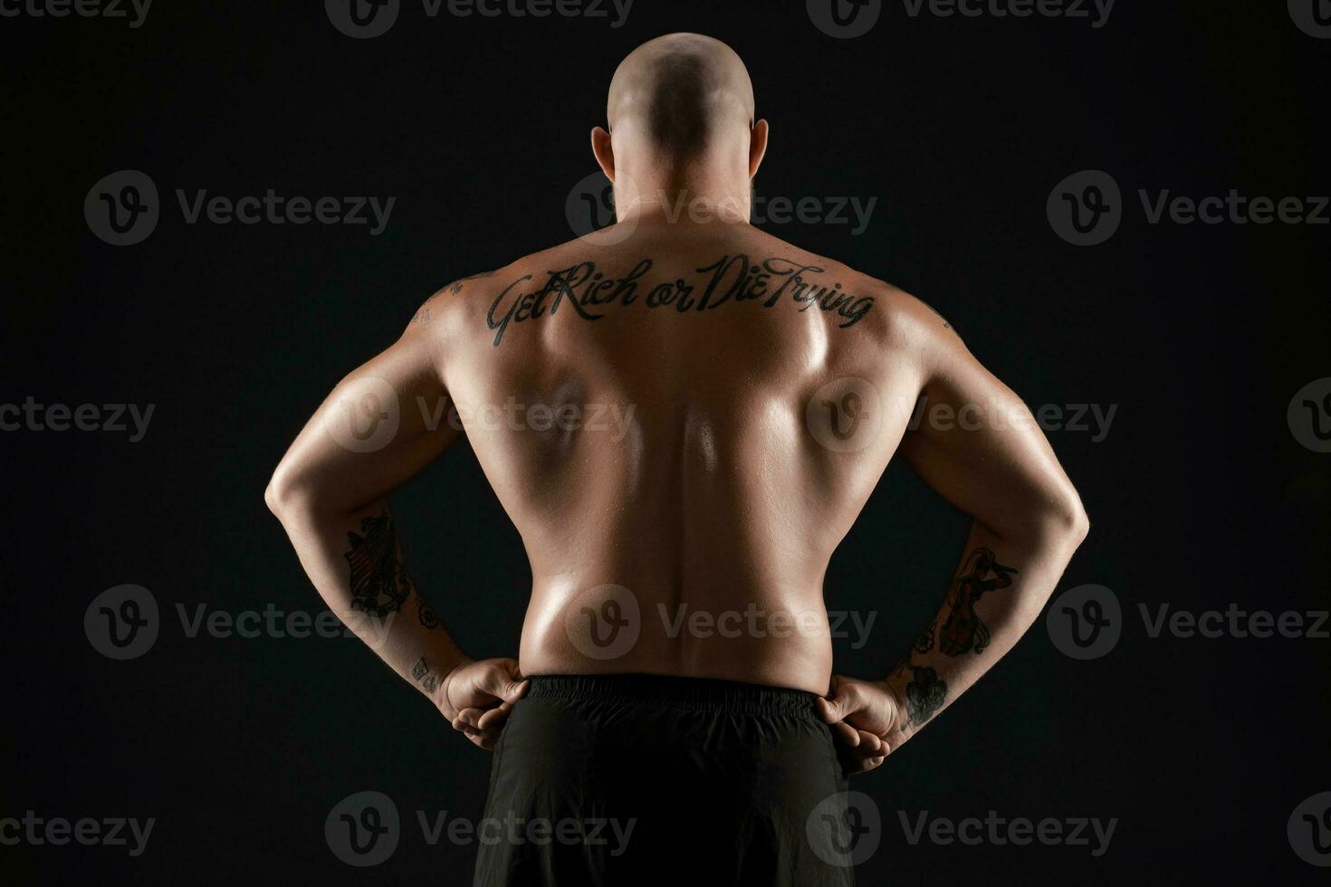 Athletic bald, bearded, tattooed man in black shorts is posing against a black background. Close-up portrait. photo