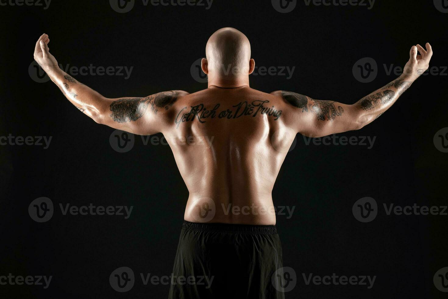 Athletic bald, bearded, tattooed man in black shorts is posing against a black background. Close-up portrait. photo