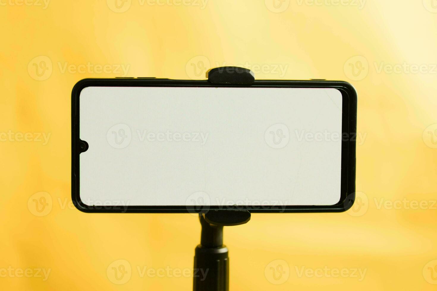 Landscape phone with white screen fixed to tripod on yellow background, for mockup design. photo