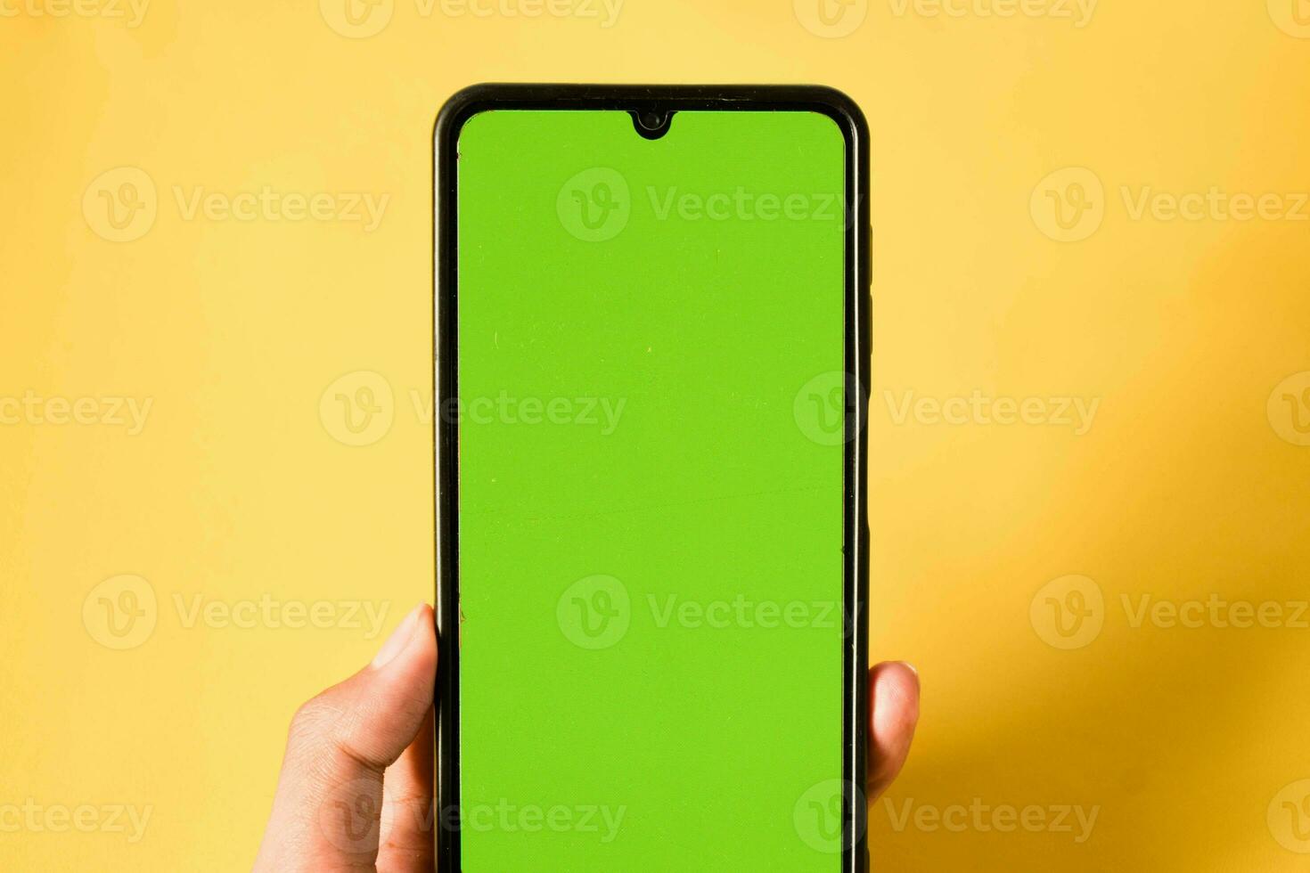 hand holding modern mobile phone green screen isolated on yellow background photo