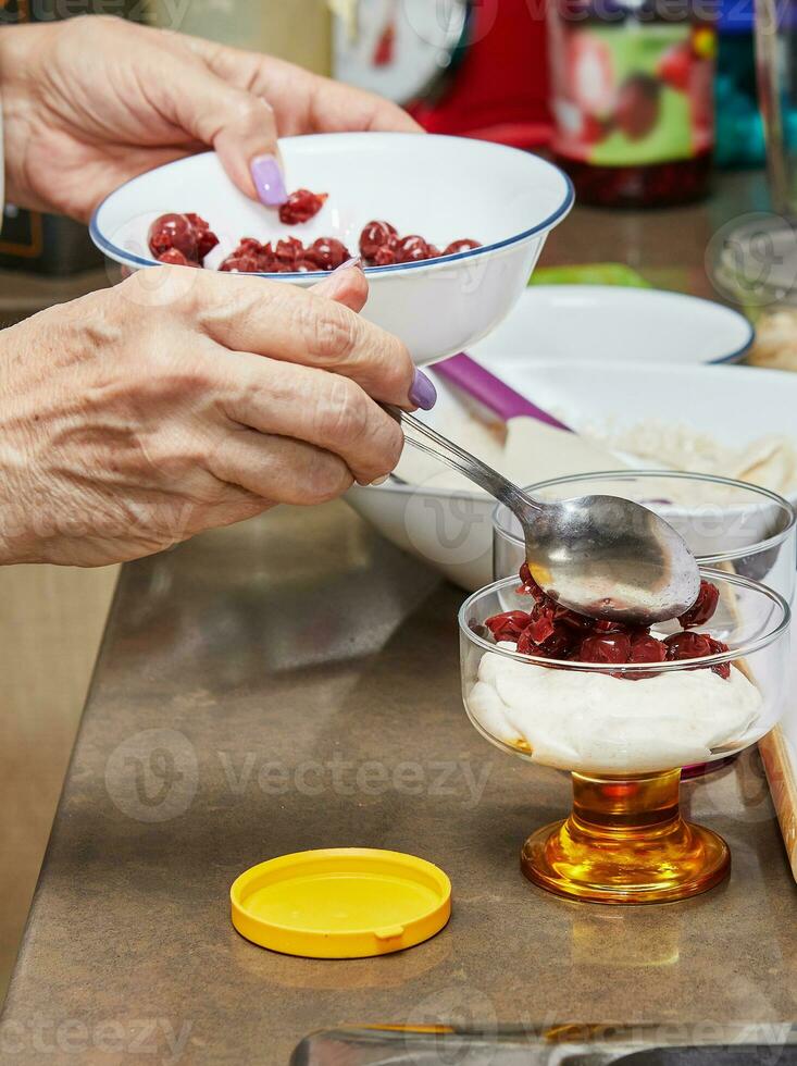 Chef preparing special dessert with fresh cream, cherry, cookies and nuts in a glass photo