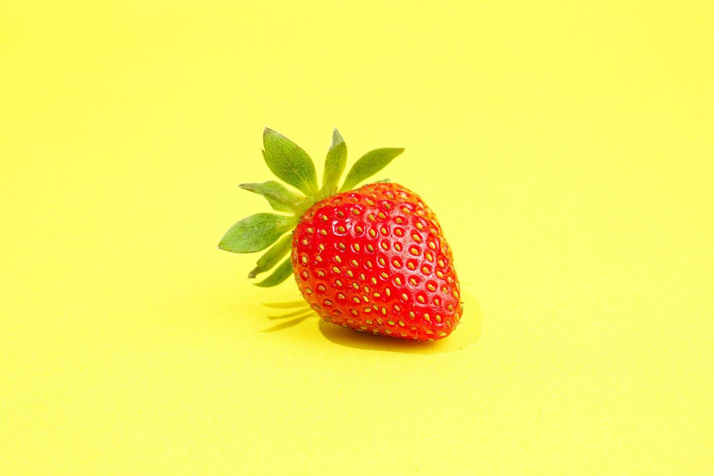 Single strawberry isolated on yellow background photo