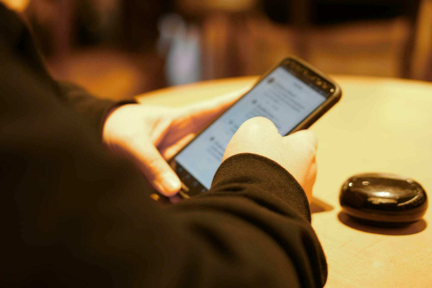 Hand of human play and touching his mobile phone on wooden table with bright lights of cafe. photo