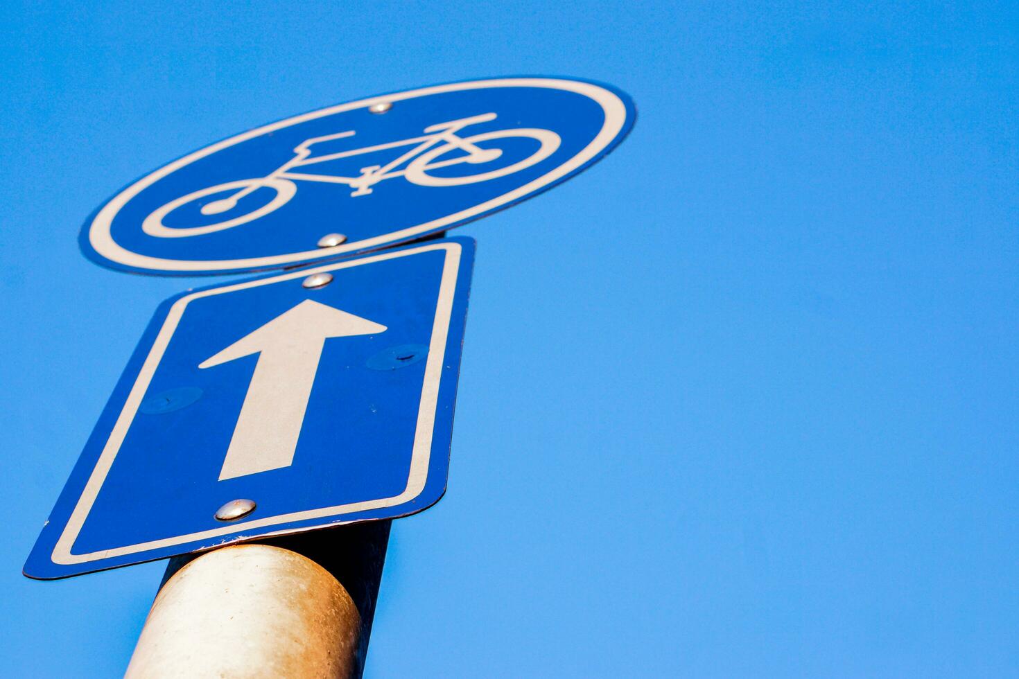 Closeup and look up view traffic signs of bicycle lane and navigation arrow on clear blue sky background. photo