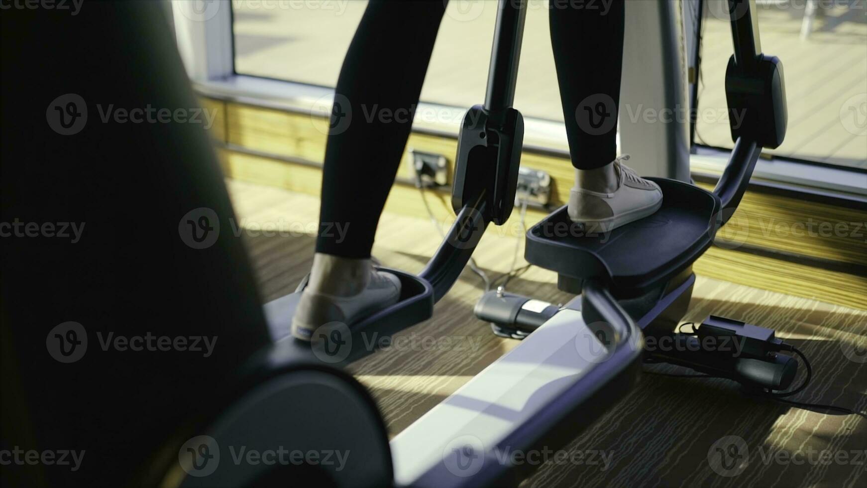 Athletic girl doing an ellipsoid in gym side view. Stock. Woman trains on an ellipsoid photo