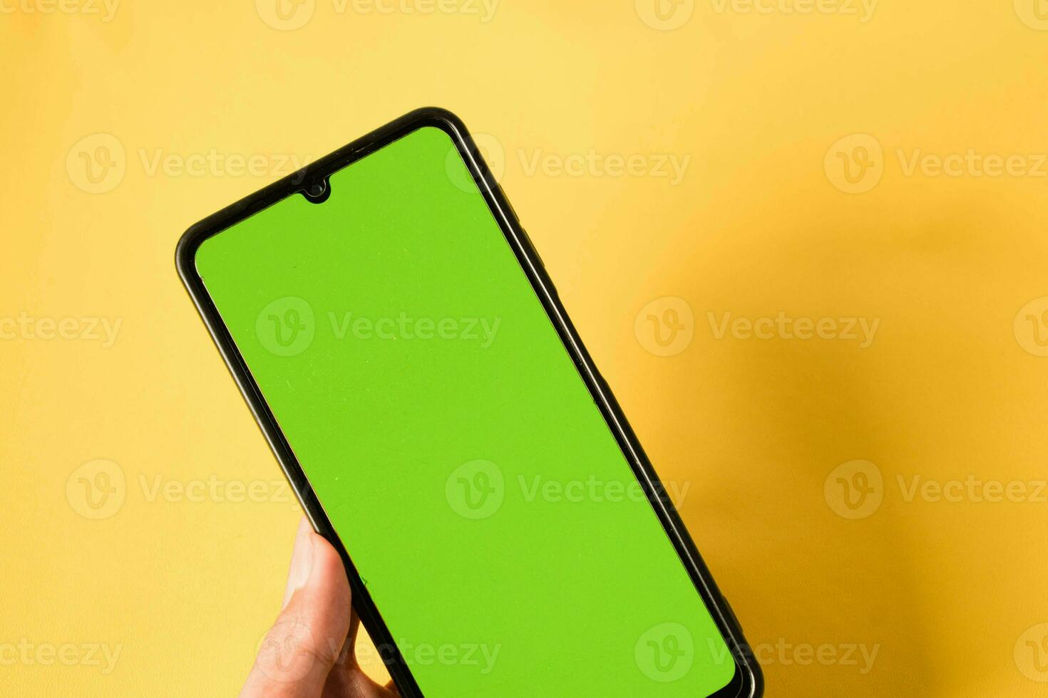 hand holding modern mobile phone green screen isolated on yellow background photo