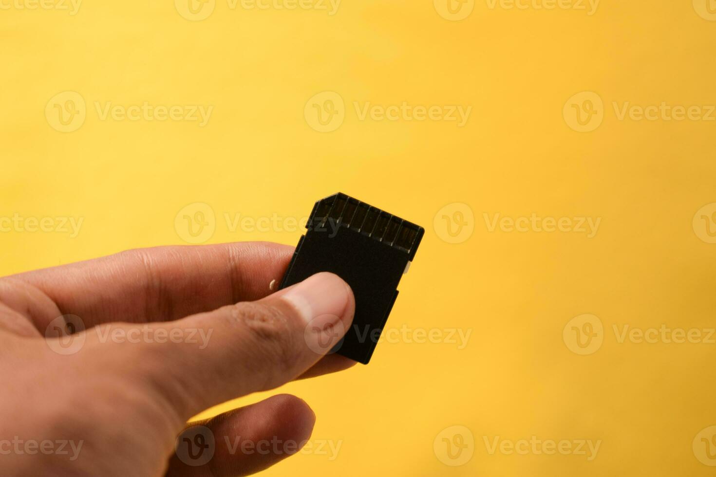 Hand holds SD Card for DSLR or Mirrorless camera on yellow background photo