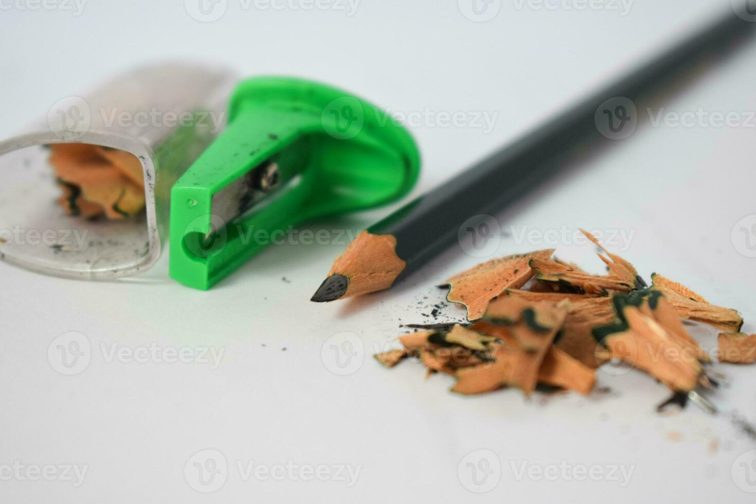 green pencil sharpener and dark green pencils, pencil shavings on white background photo